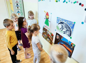 Kilkoro dzieci z grupy 3,4,5 latków oglądająca obrazki przedstawiające krasnala Hałabałę i borsuka.