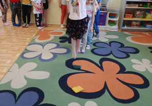 Dzieci ustawione w rzędzie, kolejno przeskakują obunóż przez woreczki gimnastyczne.