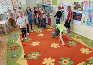 Dzieci ustawione w dwóch rzędach przechodzą na czworakach między woreczkami gimnastycznymi.