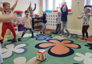Dzieci 3,4,5 letnie wykonują ćwiczenie ruchowe - pajacyka, wskazane przez obrazkową kostkę gimnastyczną.