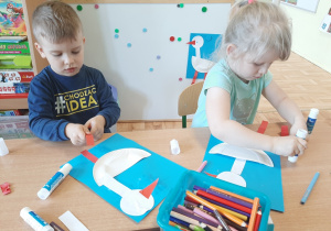 Dwoje dzieci z grupy 3,4,5 latków wykonuje obrazki przedstawiające bociana na niebieskim tle.