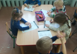 Dzieci przy stoliku malują rysunek.