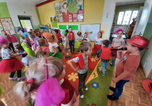Dzieci w kolorowych strojach tańczą w grupach, w parach. Chłopiec w czerwonym kapeluszu śpiewa piosenkę do mikrofonu.