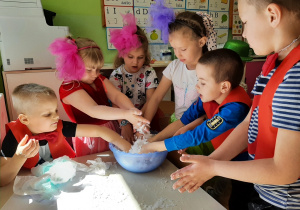 Grupa dzieci przy przedszkolnym stoliku bawi się tak zwanym sztucznym śniegiem umieszczonym w plastikowej misie.