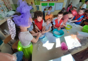 Grupa dzieci przy przedszkolnym stoliku bawi się tak zwanym sztucznym śniegiem umieszczonym w plastikowej misie oraz cieczą nieniutonowską umieszczoną w kolejnej misie plastikowej.