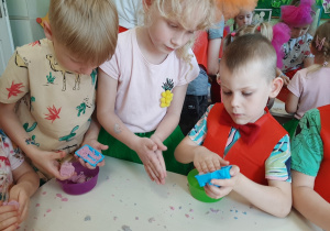 Kilkoro dzieci bawi się przy stoliku piaskiem kinetycznym wkładając go do kolorowych foremek