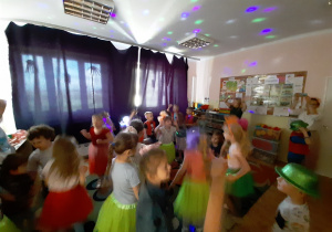 Dzieci w zaciemnionej sali przedszkolnej tańczą przy kolorowym, migającym oświetleniu- kolejne ujęcie na całą salę.