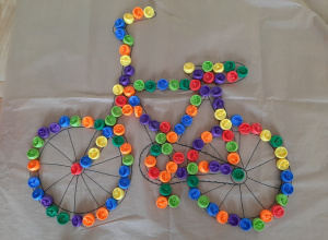 Sylweta roweru ułożona z kolorowych klocków o okrągłym kształcie na szkicu wykonanym na arkuszu papieru pakowego.