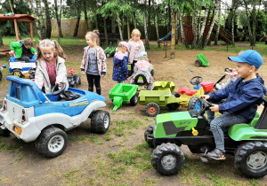 Dzieci na placu zabaw bawią się jeździkami - pojazdami.