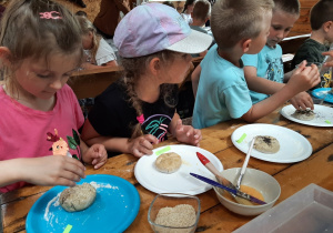 Kilkoro dzieci ozdabia uformowane kształty z ciasta chlebowego różnymi ziarnami.