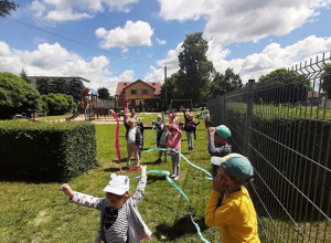 Dzieci z grupy 3,4,5 latków na przedszkolnym placu zabaw badają kierunek wiatru za pomocą pasków bibuły.