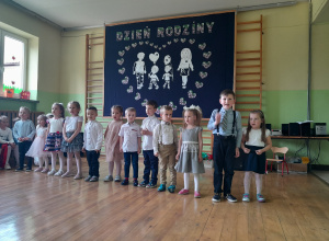 Grupa dzieci z grupy 3-4 latków stoi w rzędzie i recytuje wiersze dla rodziców