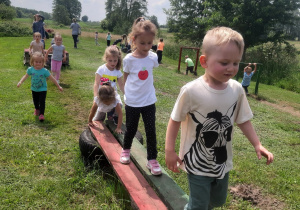 Dzieci pokonują tor sprawnościowy przechodząc przez drewniane bale