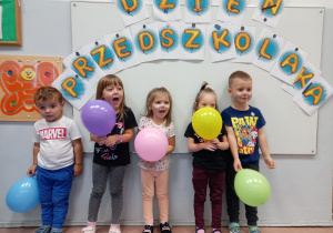 Przedszkolaki z balonami na tle tablicy z napisem