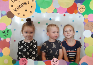 3 dzieci pozuje w foto ramce z kolorowych kropek