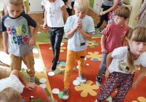 Dzieci z grupy 5,5 latków uczestniczą w zabawie ruchowej z wykorzystaniem kolorowych kół wyciętych z papieru.