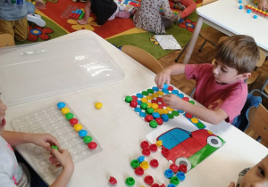 Dzieci bawią się plastikowymi, kolorowymi klockami w kształcie kół. Umieszczają je na planszy według wzoru.
