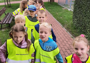 grupa dzieci 5,6 letnich ubrana w kamizelki odblaskowe stoi na chodniku przed budynkiem przedszkola.