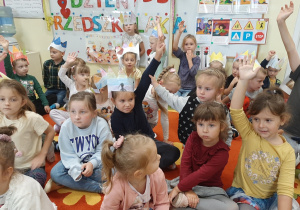 Dzieci siedzą na dywanie, biorą udział w quizie wiedzy o przedszkolu. Podnoszą rękę gdy znają odpowiedź.