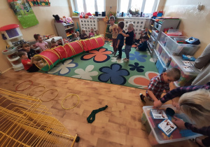 Chłopcy z grupy 3,4,5 latków na sali przedszkolnej pokonują tor przeszkód by dostać legitymację super chłopaka. Reszta grupy siedzi na dywanie i dopinguje uczestników.