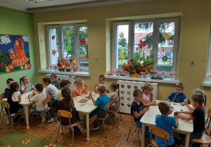 Dzieci z grupy 5,6 latków siedzą w sali przy stolikach, jedzą słodki poczęstunek.