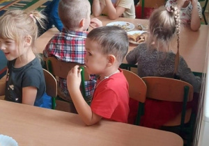 Dzieci z grupy 3,4, 5latków siedzą w sali przy stolikach, jedzą słodki poczęstunek.
