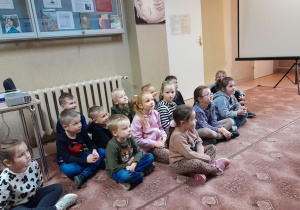 Dzieci siedzą na dywanie i słuchają opowieści bibliotekarki o wynalazcach