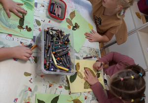 Dzieci przy stolikach wykonują zwierzaki - cudaki. Tworzą je z liści naklejanych na karton. dorysowują elementy kredkami.