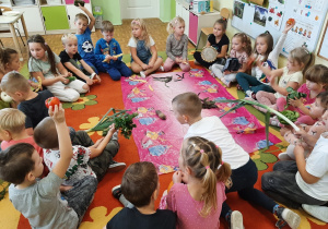 Dzieci siedzą w kole na dywanie. W środku koła rozłożone są warzywa. Dzieci dotykają, badają wybrane przez siebie warzywa.