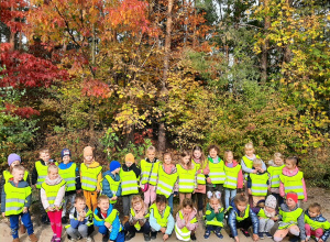 Dzieci na spacerze w lesie. Pozują na tle drzew w jesiennych kolorach.
