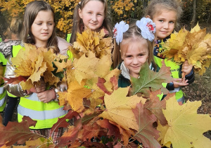 4 dziewczynki prezentują duży bukiet z liści jesiennych.
