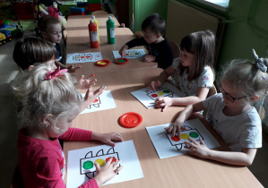 Dzieci przy stolikach malują farbami sygnalizator świetlny.