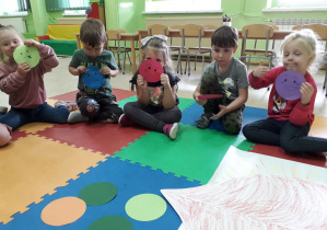 Dzieci na dywanie prezentują różne emotki.
