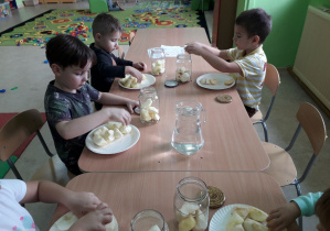 Dzieci przy stolikach wkładają jabłka do słoików, przygotowują kompot.