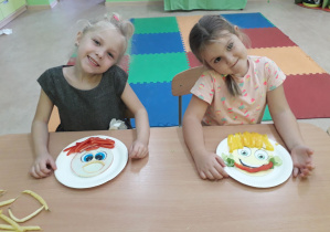 Dziewczynki przy stolikach prezentują swoje warzywno-owocowe portrety.