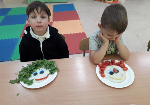 Chłopcy przy stolikach prezentują swoje warzywno-owocowe portrety.