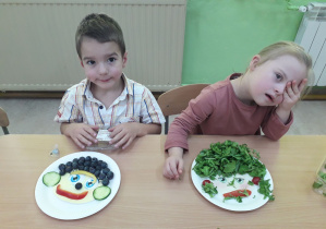 Dzieci przy stolikach prezentują swoje warzywno-owocowe portrety.