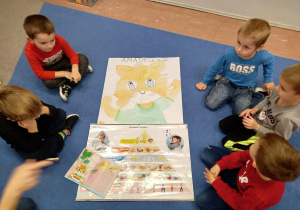 Przedszkolaki siedzą na dywanie i przyglądają się plakatowi z piramidą żywienia
