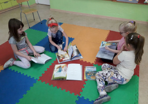 Dzieci na dywanie oglądają książki z basniami.