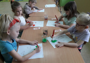 Dzieci przy stolikach malują farbami kontury Włoch barwami narodowymi.