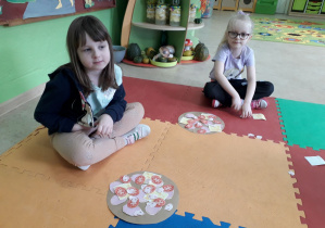 Dziewczynki na dywanie prezentują pracę plastyczną: "Pizza".