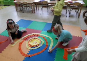 Dzieci na dywanie układają z kolorowej bibuły Układ Słoneczny.
