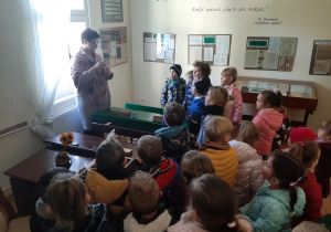 Dzieci zwiedzają Izbę Zbiorów Oświatowych, przewodnik prezentuje pióro i kałamarz.