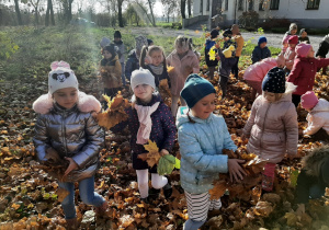 Grupa dzieci w bronowskim parku zbiera kolorowe liście.