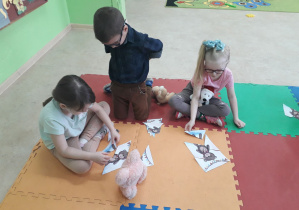 Dzieci na dywanie układają pocięty obrazek misia w całość.