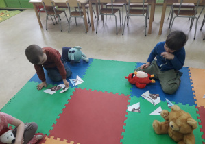 Dzieci na dywanie układają pocięty obrazek misia w całość.