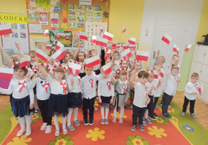 Dzieci pozują do fotografii machając polskimi flagami.