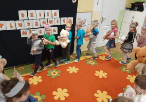 Dzieci z grupy 5,6 latków tańczą w kole trzymając w rękach misie maskotki.