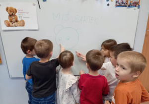 Dzieci z grupy młodszej przy tablicy podczas nadawania imienia wspólnie narysowanemu misiowi