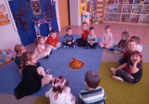 Dzieci siedzą w kole w magicznym kręgu podają sobie andrzejkowy płomień